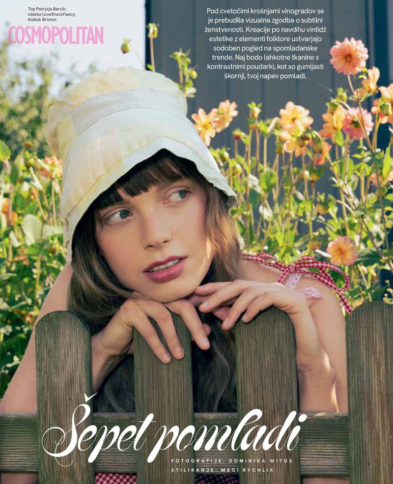 Young woman with a hat leans against a wooden fence amidst flowers in a garden setting for a fashion editorial magazine cover.