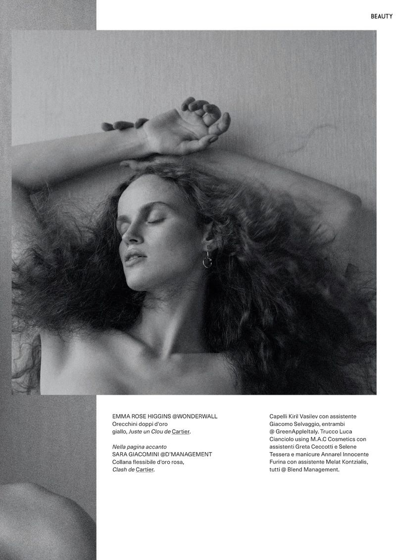 Black and white portrait of a serene adult female model with closed eyes and curly hair, lying against a neutral wall, beauty editorial.