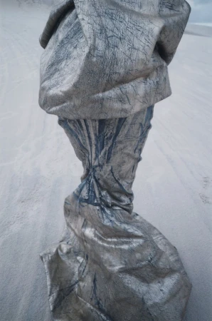 Abstract draped fabric sculpture with a cracked texture, casting shadows on a grainy surface, creating a surreal, otherworldly visual.