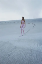 Model wearing pink matching set walking down a white sand dune under an overcast sky for Harper's Bazaar U.S.