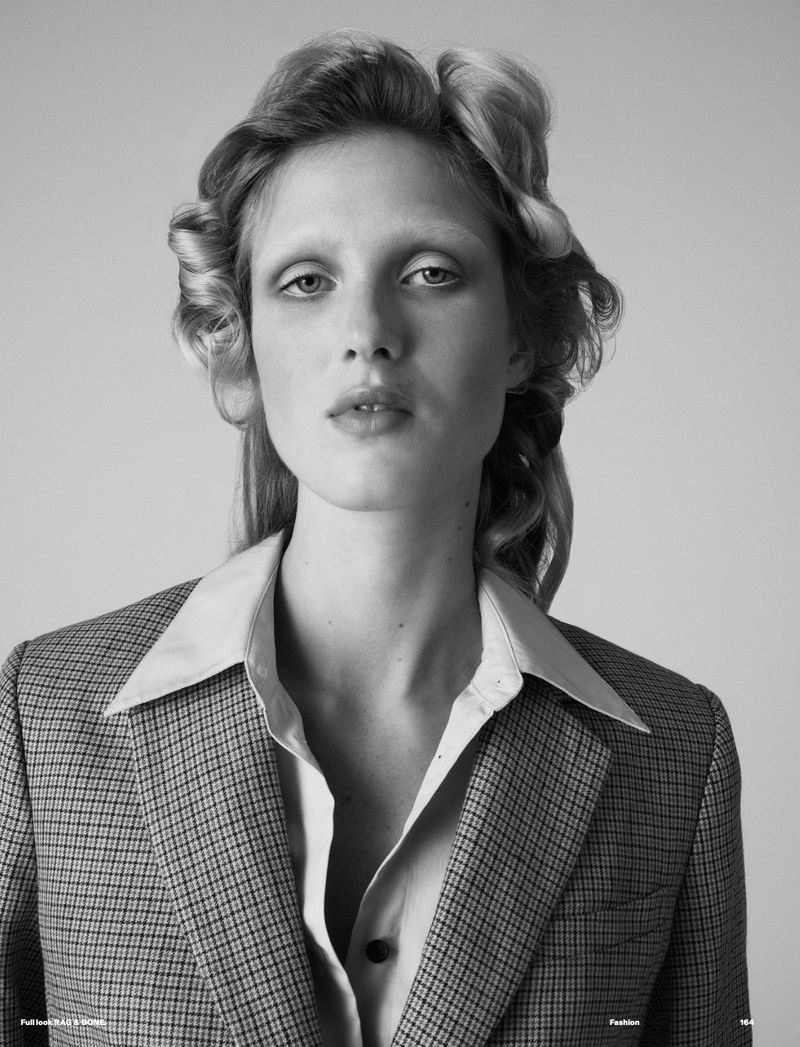 Black and white portrait of a fair-skinned woman wearing a houndstooth blazer, styled with hair rollers and a button-down shirt.