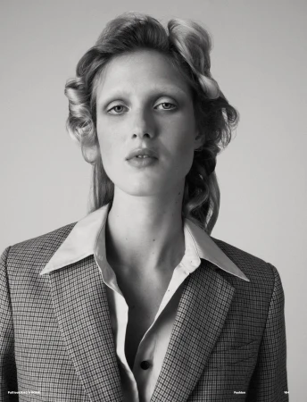 Black and white portrait of a fair-skinned woman wearing a houndstooth blazer, styled with hair rollers and a button-down shirt.