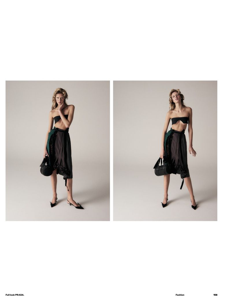 Fashion editorial shot of a woman in a black tube top and dark skirt, holding a black purse, posing in a light-colored studio.