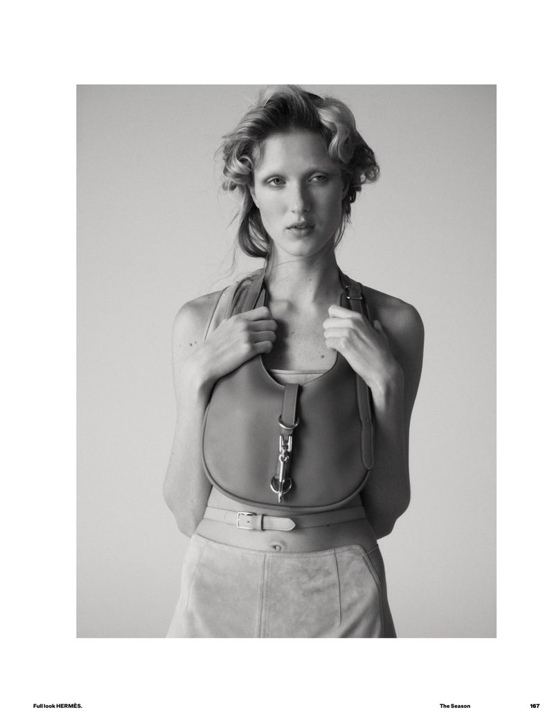 Monochrome portrait of a model posing with a leather handbag and a belt, against a neutral background, in a fashion editorial.
