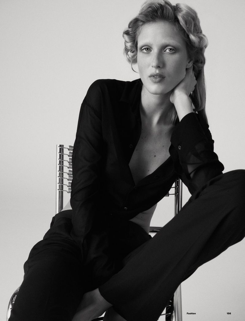 Monochrome fashion portrait of a blonde adult woman with hair rollers, posing on a chrome chair in a black shirt and pants.