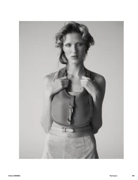 Black and white portrait of a female model holding a leather handbag against a plain studio background for Muse Magazine.