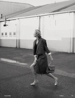 Model Vakare Steputyte in a grey cropped blazer and skirt holding a handbag outdoors against a building exterior for Muse Magazine