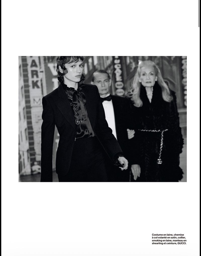 Editorial fashion shot featuring an adult female model in a black blazer and satin blouse, with two adults walking in the background.