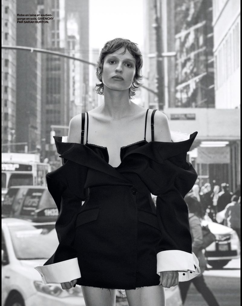 Monochrome portrait of a model in a black off-the-shoulder dress with oversized sleeves, posing outdoors in a city street setting.