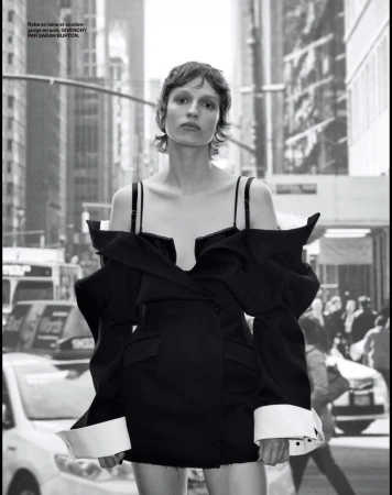 Monochrome portrait of a model in a black off-the-shoulder dress with oversized sleeves, posing outdoors in a city street setting.