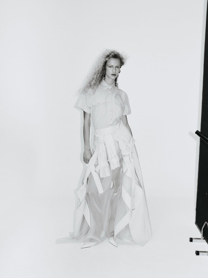Fashion photography features a woman in a light shirt and skirt, posing in a photo studio with bright lighting and a minimalist background.