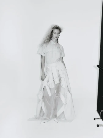 Fashion photography features a woman in a light shirt and skirt, posing in a photo studio with bright lighting and a minimalist background.