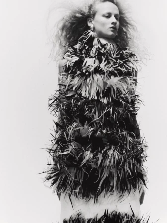 Monochrome fashion editorial portrait of a woman wearing a textured feather dress against a seamless white background.