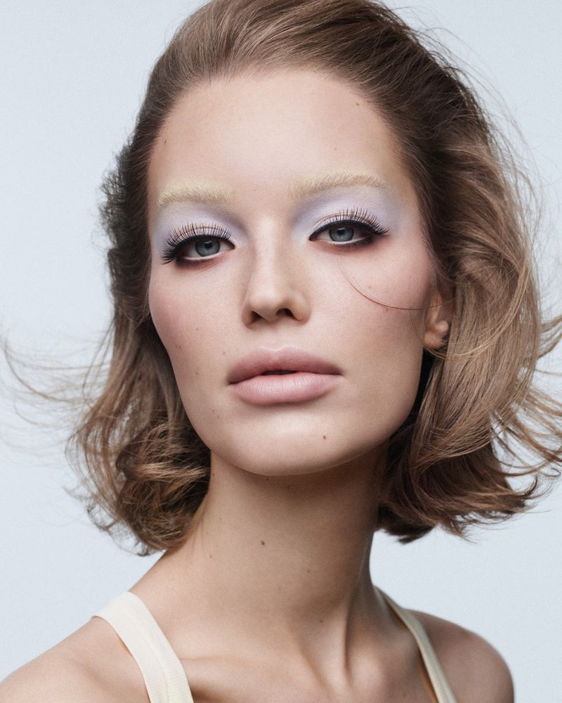 Beauty shot portrait of a woman with blonde bob haircut and light-color makeup against a neutral background in a photo studio.