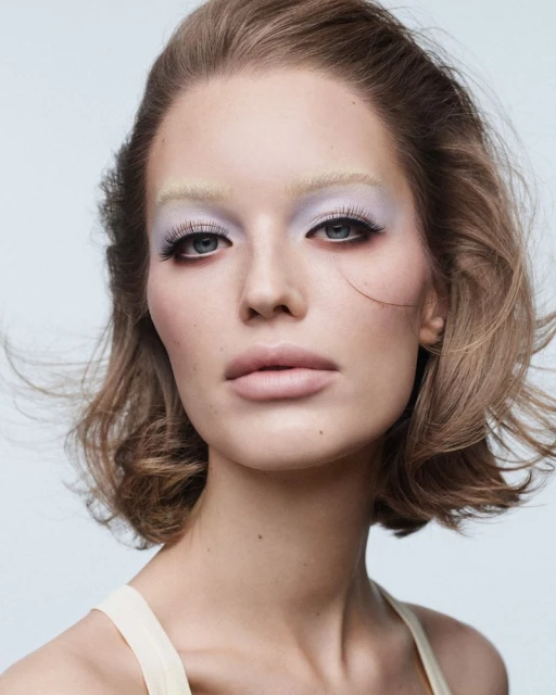 Beauty shot portrait of a woman with blonde bob haircut and light-color makeup against a neutral background in a photo studio.