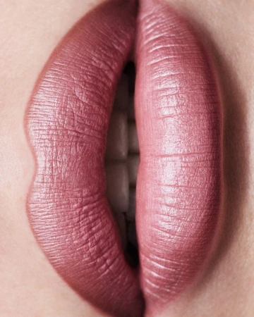 Close-up of woman's lips with mauve lipstick and visible teeth. Beauty shot emphasizing the texture and color of the makeup.