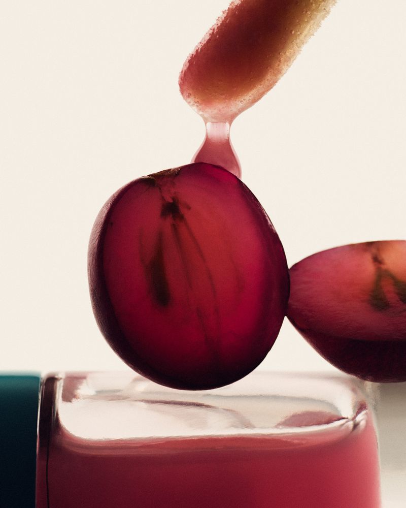 Macro shot of a sliced red grape next to a jar with red liquid, highlighting food photography, fresh ingredients, and vibrant colours.