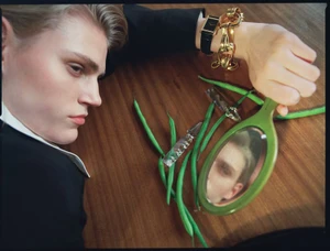 Model lying on wooden table holding green hand mirror surrounded by green beans