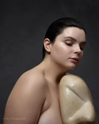 Portrait of a model with slicked-back dark hair holding a smooth sculpted ceramic prop against a dark textured background.