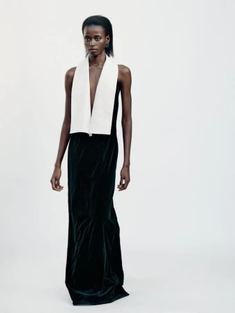 Elegant black female model poses in a long, dark dress with a contrasting white stole in a brightly lit studio setting.