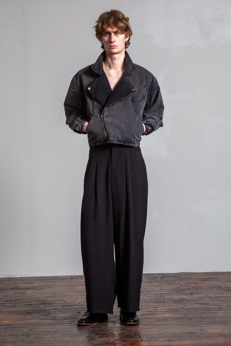Full-length studio shot of a young adult man wearing a gray denim jacket with black dress pants and black leather dress shoes.