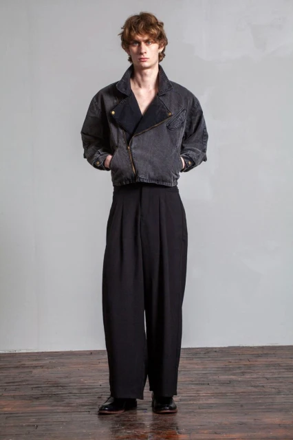 Full-length studio shot of a young adult man wearing a gray denim jacket with black dress pants and black leather dress shoes.