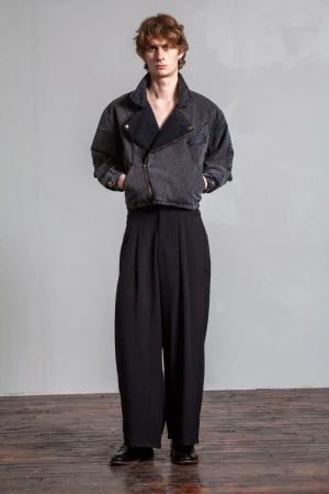 Full-length studio shot of a young adult man wearing a gray denim jacket with black dress pants and black leather dress shoes.