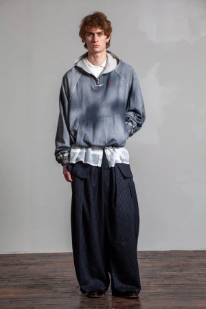 Full-length shot of an adult male fashion model wearing an oversized hoodie and wide-legged striped pants in a photo studio setting.