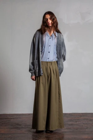 Model with long hair wearing an oversized grey cardigan over a light blue button-up shirt and wide olive trousers.