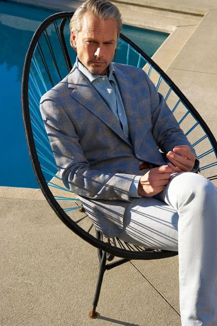 Adult male seated in modern chair outdoors in light blue suit. Daytime portrait with architectural and pool elements in the background.