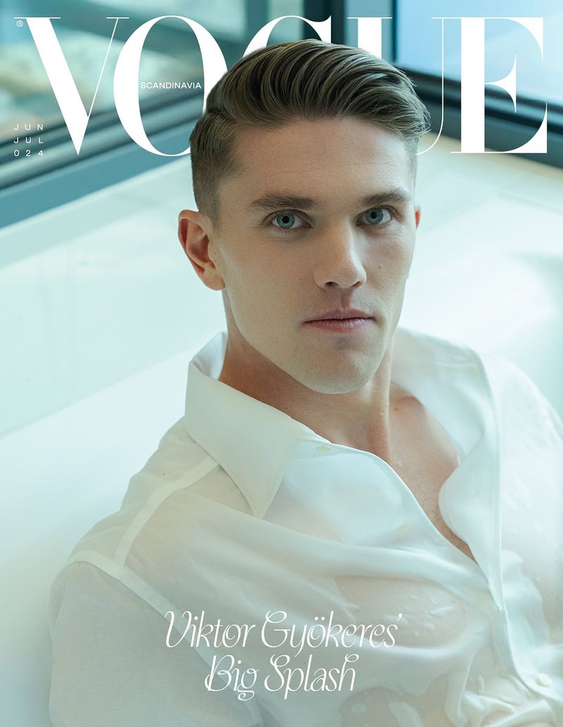 Close-up studio shot of a young adult male model with short brown hair wearing a sheer white shirt, set against a light-colored backdrop.
