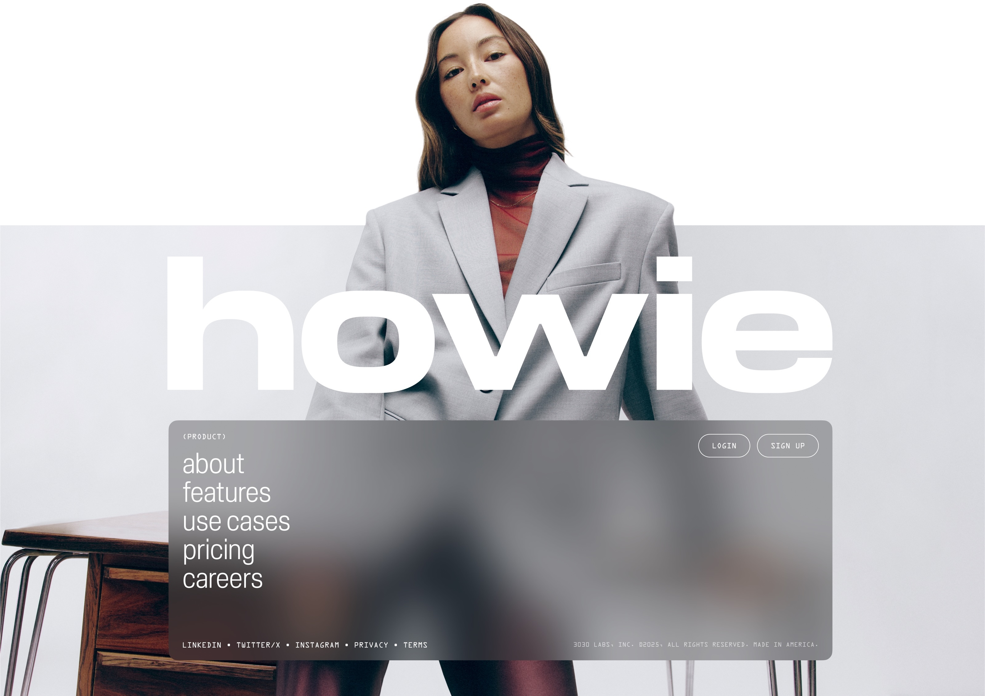 Adult female in gray blazer standing in front of web page mockup with white sans-serif text, desk visible on left.