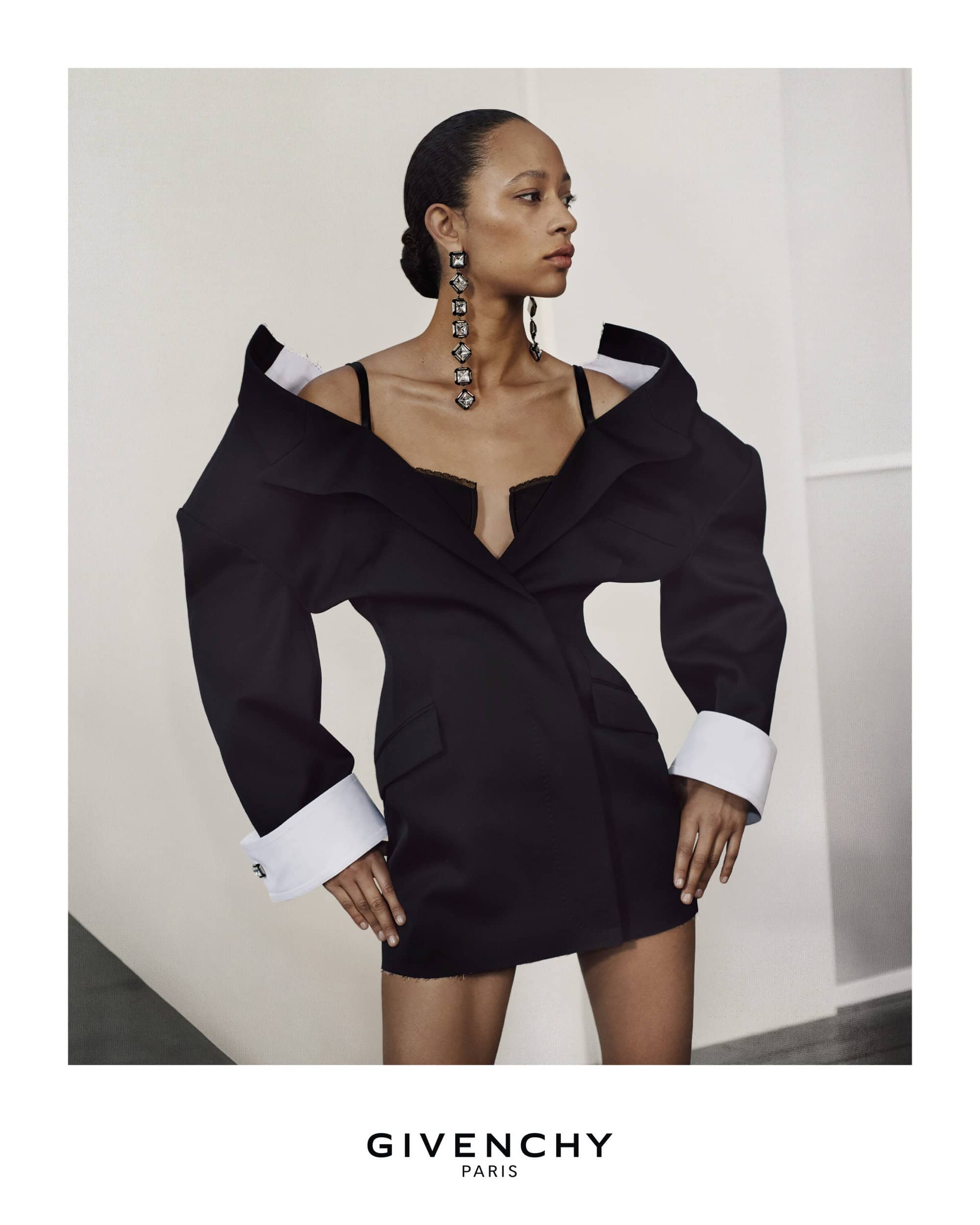 Elegant woman wearing oversized black blazer dress and statement earrings in a studio setting. Fashion and beauty shot.