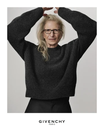 Older woman with blonde hair poses in a fashion shot, wearing a dark grey sweater against a light grey background, advertising Givenchy Paris.