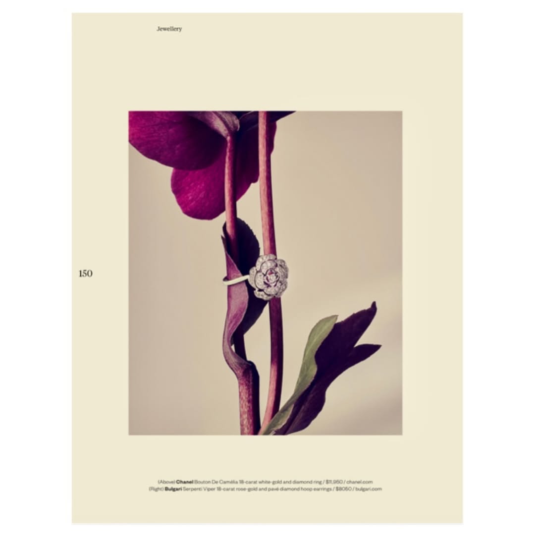 Floral diamond ring on a stem with purple leaves against a light beige background in a studio shot for a jewellery advertisement.