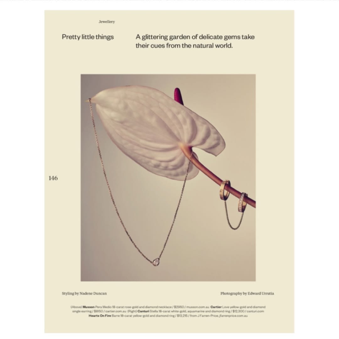 Editorial shot of white anthurium flower with gold necklace and rings. Jewelry advertisement features delicate, natural-world-inspired aesthetic.