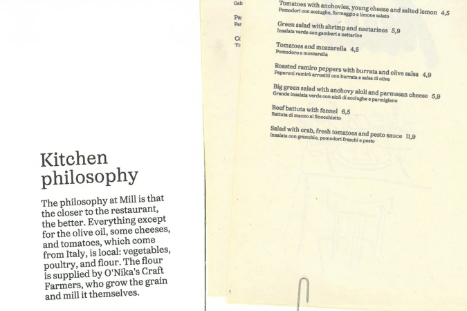 Close-up of two printed pages: one outlining a restaurant's kitchen philosophy, and the other listing menu items with prices.
