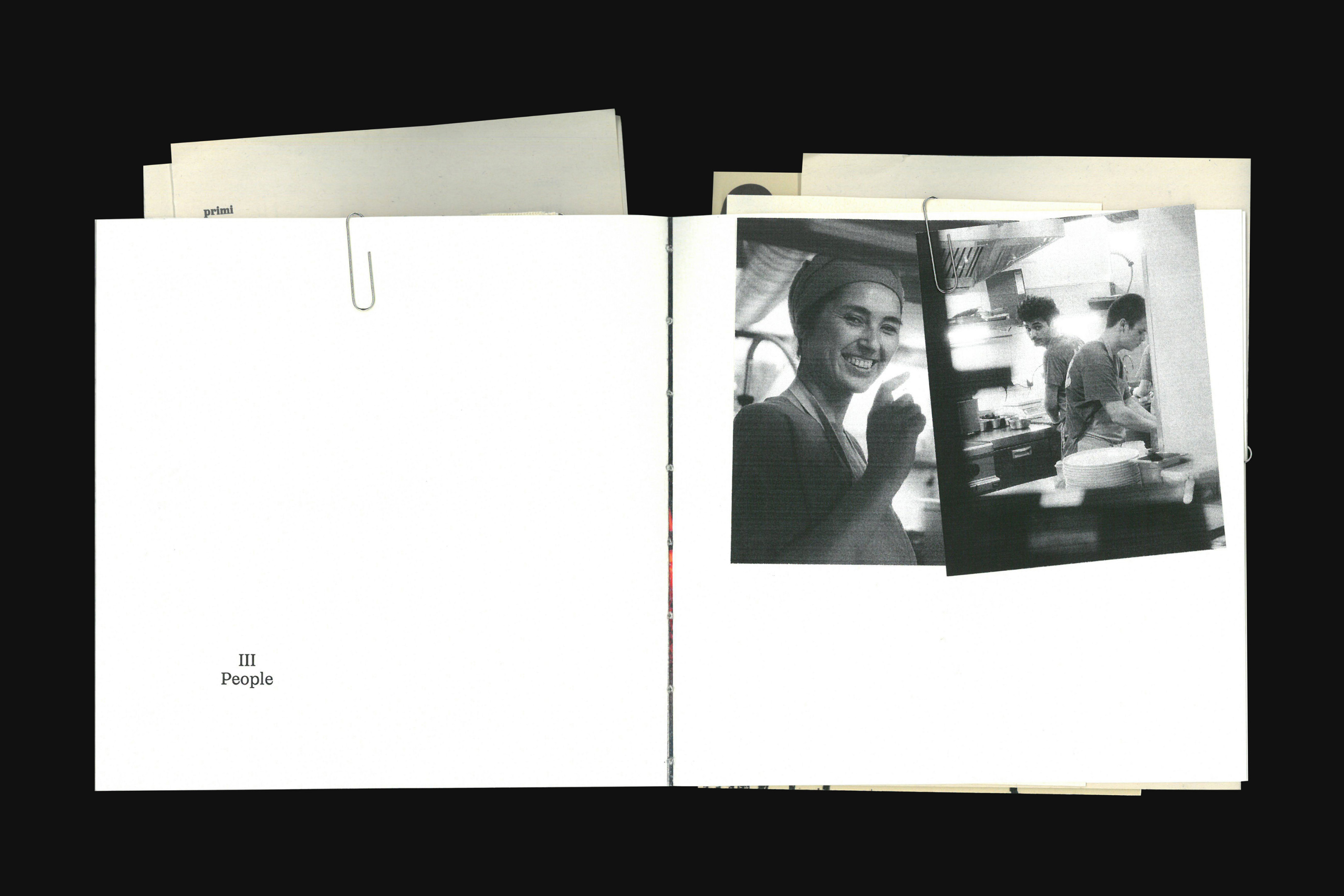 Monochrome image inside a book showcasing an adult woman smiling in a kitchen, with two adults working in the background.