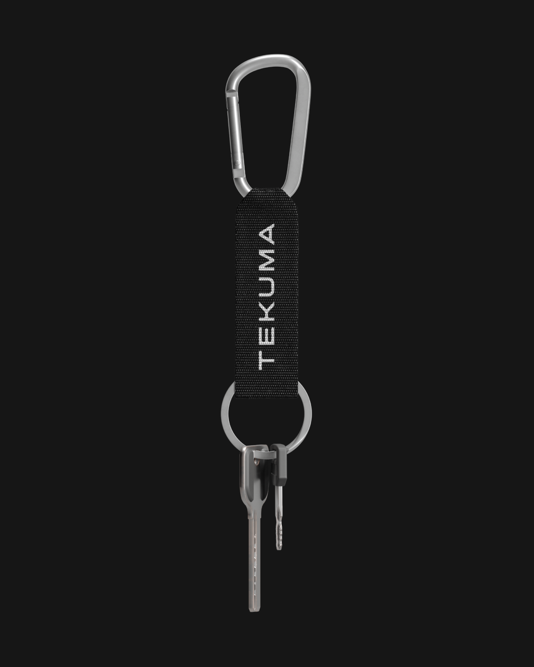 Close-up studio shot of a silver-tone carabiner attached to a black strap with 'TEKUMA' in white text, holding two keys, against black.