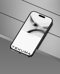 A sleek smartphone displaying the Tekuma brand interface resting diagonally on a dark metallic grey paneled surface