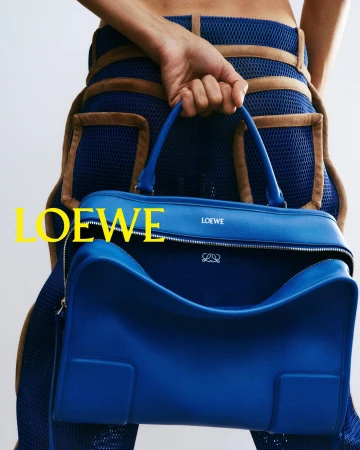 Close-up studio shot of a blue leather Loewe handbag held by a slender woman with bare midriff wearing matching blue apparel.