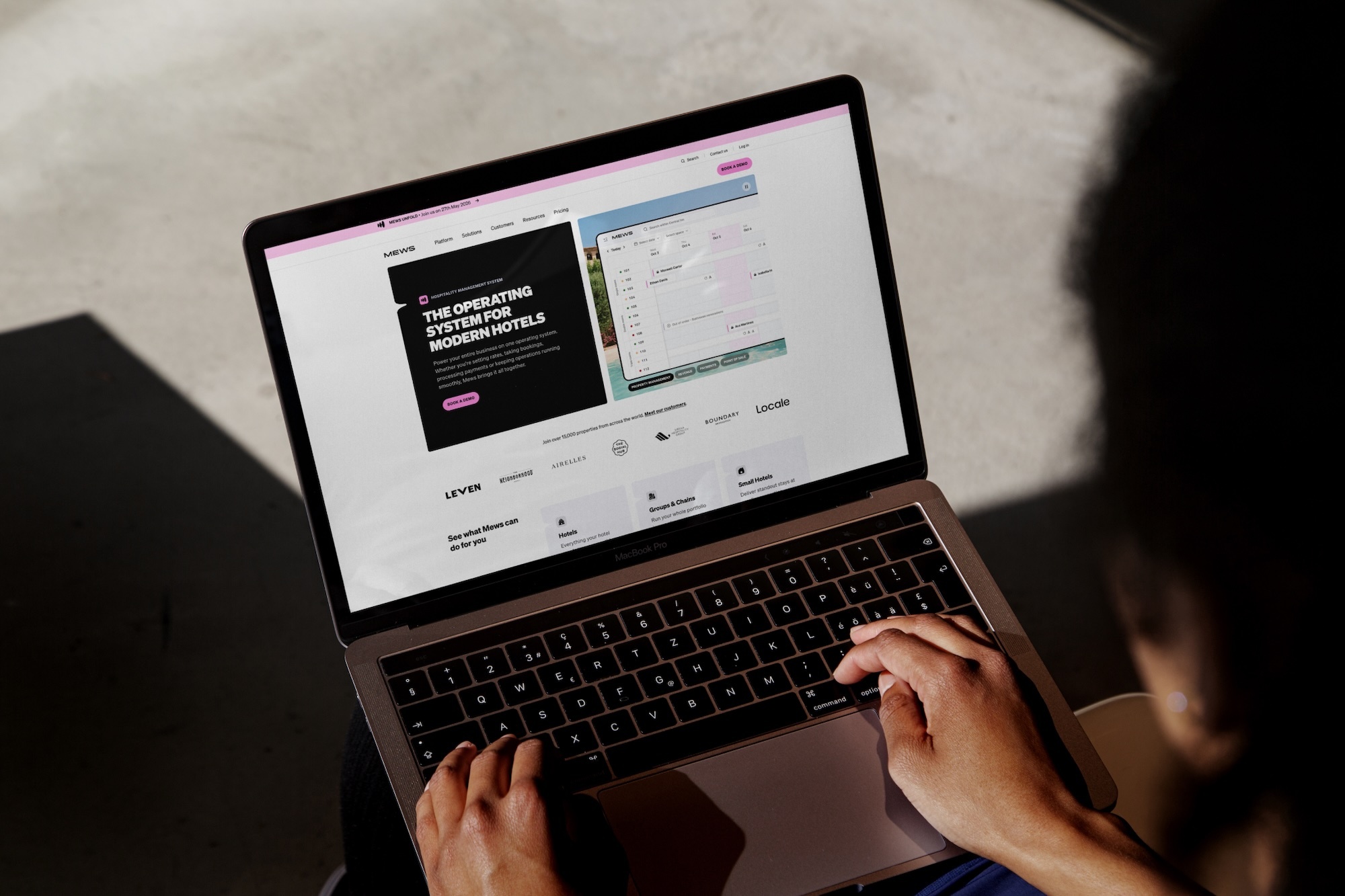 Person types on a rose gold MacBook Pro, typing on the keyboard, against a gray textured background, with visible screen content.