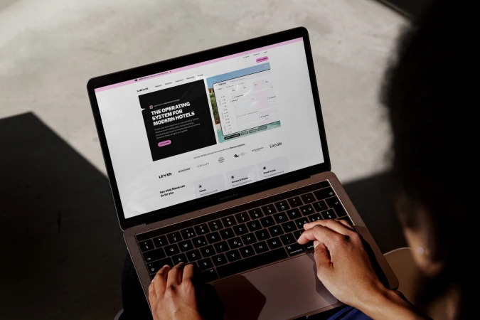 Person types on a rose gold MacBook Pro, typing on the keyboard, against a gray textured background, with visible screen content.