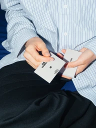 Close-up of hands holding white business cards wearing a blue striped button-down shirt and black trousers.