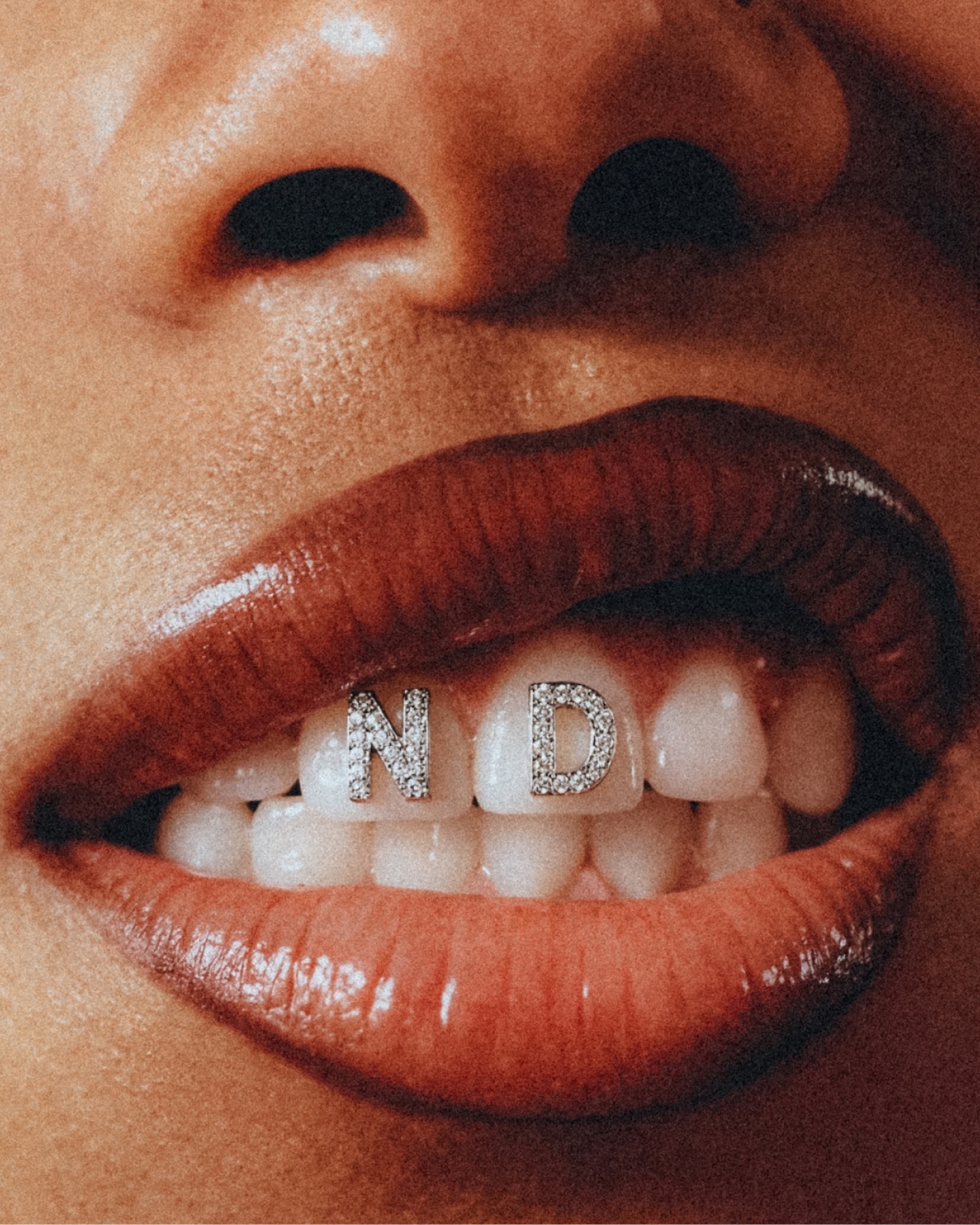 Macro shot of an adult woman's open mouth featuring red lipstick and diamond dental jewelry spelling ND on her front teeth.