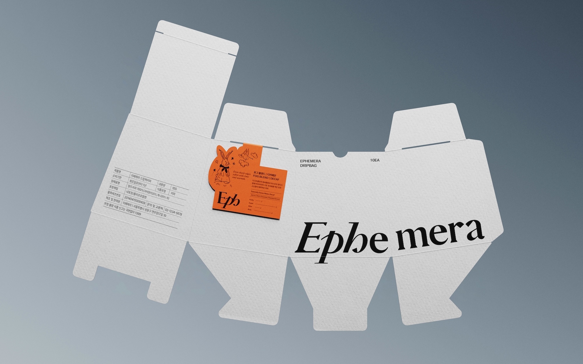 Unfolded white product box with orange Ephemera brand label. Packaging features die-cut design for easy assembly on light grey backdrop.