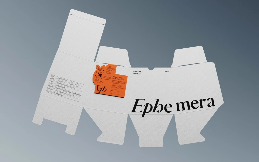 Unfolded white product box with orange Ephemera brand label. Packaging features die-cut design for easy assembly on light grey backdrop.