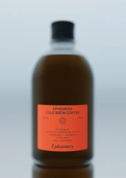 Amber cold brew coffee bottle with a bright orange label set against a minimalist light background