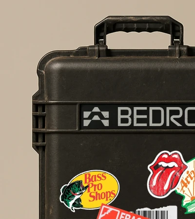 Black hard case with handle and various stickers, including Bass Pro Shops and a Rolling Stones tongue logo, in a studio setting.