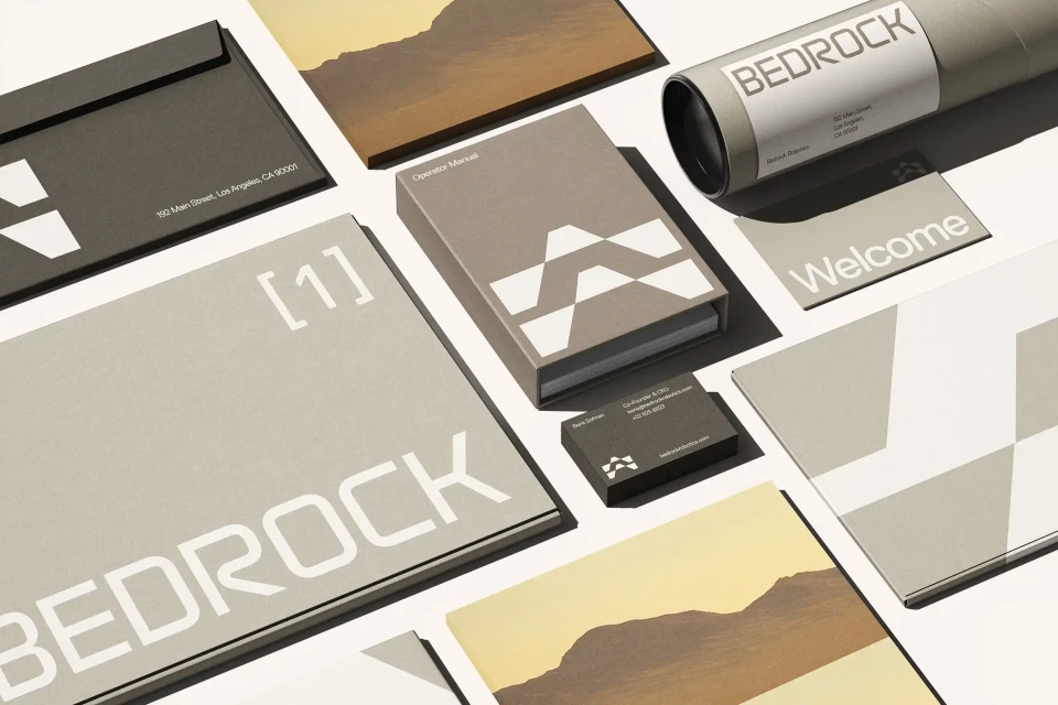 Flat lay of Bedrock-branded stationery including envelopes, cards, and manuals, in grey, white, and brown tones on a white backdrop.